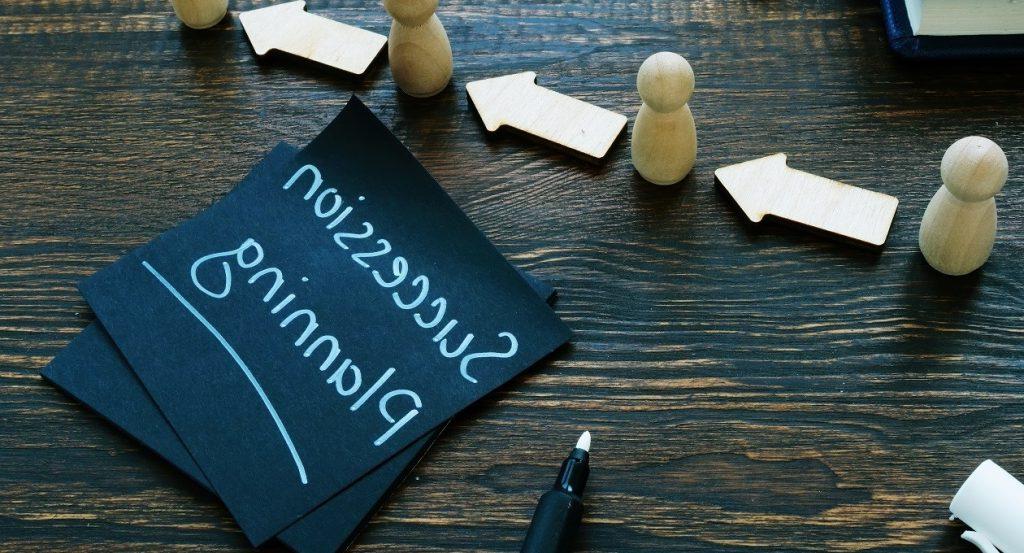 Wooden figures and arrows on a table pointing towards cards labeled "Succession Planning."